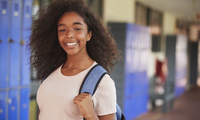 Happy black teenage girl smiling in high school corridor
